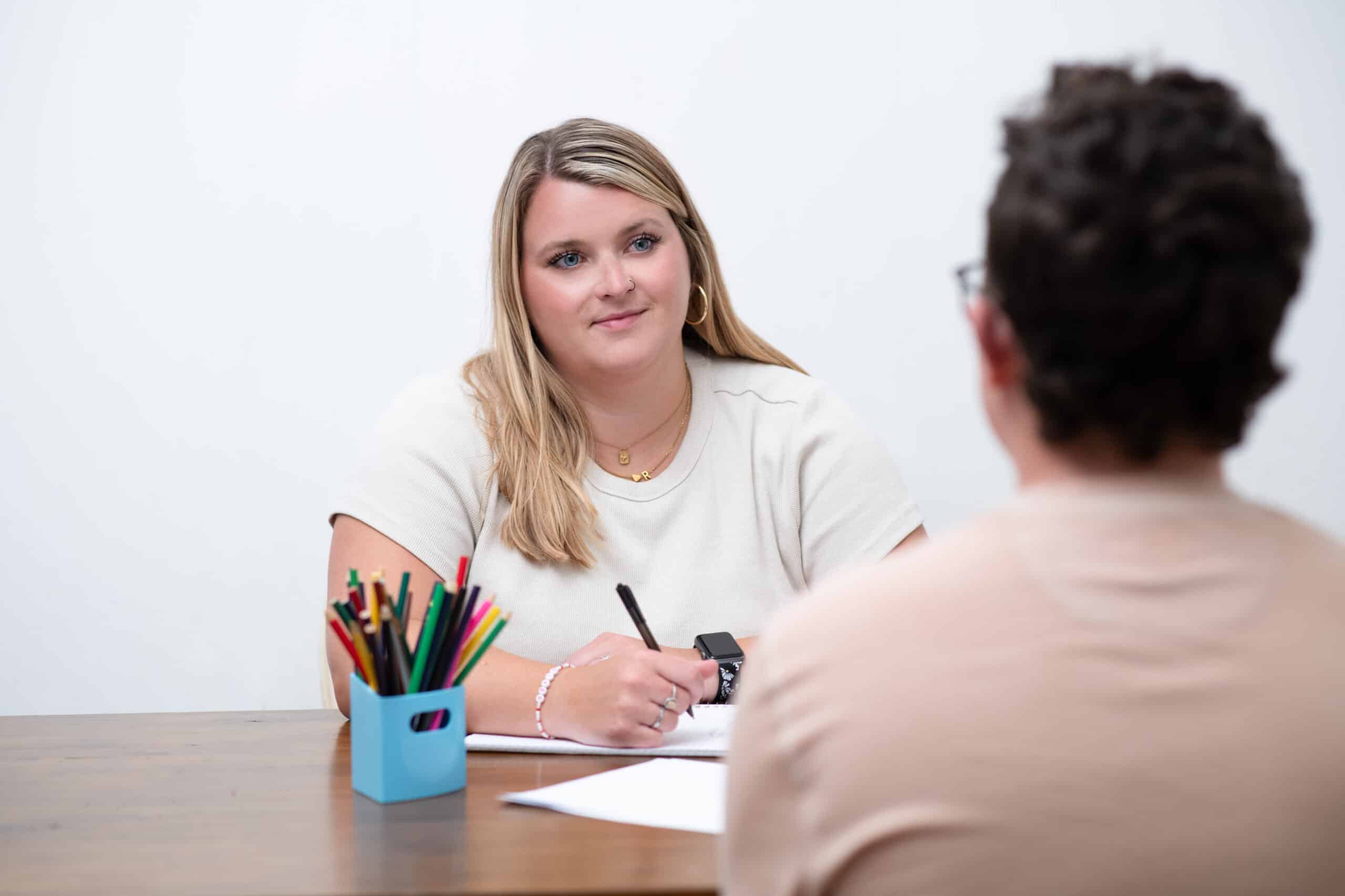 Woman taking notes at table while speaking to man